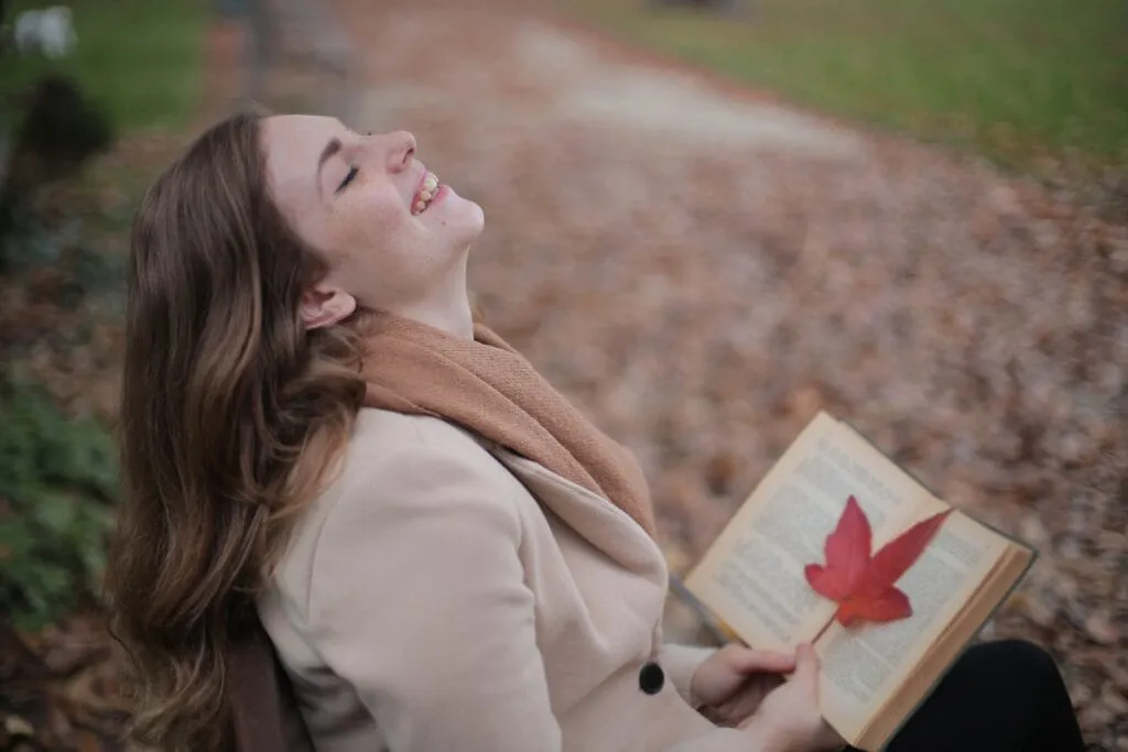 Smiling woman with an open book and leaf, reflecting a positive mindset and joy in nature.
